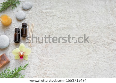 Spa concept on white soft towel background with natural cosmetic products, flower, green leaves and zen like stones, top view, copy space.