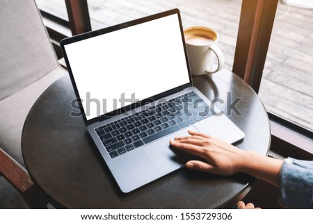 Mockup image of a hand using and touching on laptop touchpad with blank white desktop screen with coffee cup on the table 