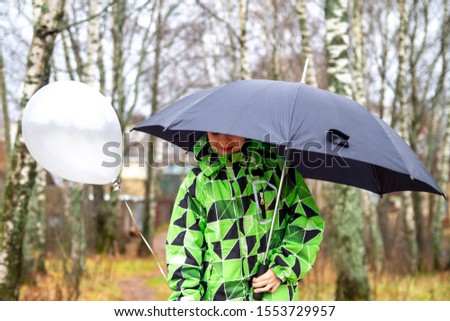 A teenage boy walks with an umbrella and a grey balloon in the rain. Sad boy. It was a cold, rainy autumn.