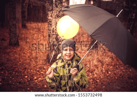 A teenage boy walks with an umbrella and a Golden yellow balloon in the rain. The balloon is like the sun. The boy laughs, rejoices, is happy. A child hides a balloon under an umbrella.