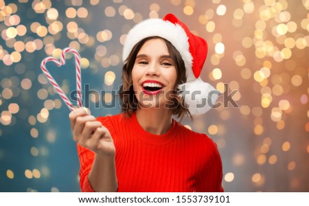 christmas, holidays and people concept - happy smiling young woman in santa helper hat with candy canes over grey background