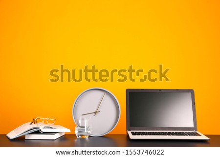 Blank screen laptop computer, various supplies on wooden desk over bright yellow wall background with a lot of copy space for text. Creative workspace. Close up shot of table w/ computer & stationery.