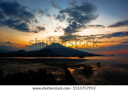 sunset and sunrise are the natural beauty at the end of the night and at dusk giving the perfect color to the sky so the clouds look beautiful to be seen with the beach set against a mountain.