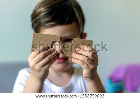Cute boy holding in hands two puzzle pieces .Three years old boy merging together two matching puzzle pieces,leaning at home.Portrait of kid connecting puzzle piece.Development,training concept. 
