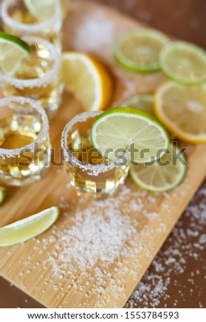 Gold tequila with salt, lemon slices and lime on a wooden background. 
Agave Mexican Alcoholic Drink.