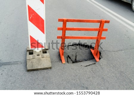 Warning sign and a hole on the road. Dangerous place.