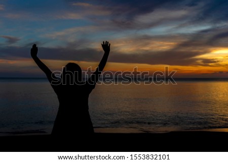 Silhouette of a woman are standing raise two hands at the seaside and the sunset is background.