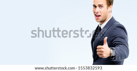Happy excited businessman showing thumbs up gesture, isolated over grey background. Business success concept picture. Copy space for some text or advertise slogan.