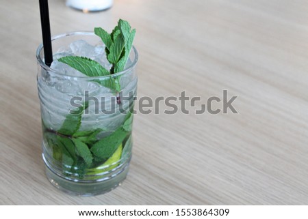 Glass of mojito cocktail on wooden table with black straw, ice and mint leaf. Copy space for text. Alcoholic or nonalcoholic and soft drink in the bar or restaurant or cafe. Picture for menu