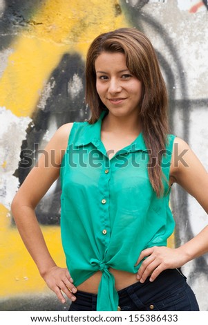 Portrait of a young Latino Lady, standing in front of yellow graffiti