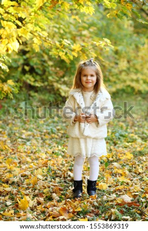 Cute little daughter standing in autumn park a