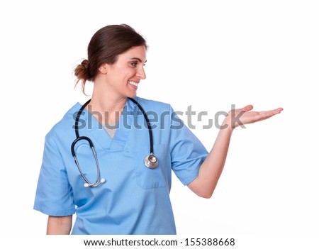 Portrait of a pretty hispanic nurse standing, looking at her left, palms out, to copyspace on white background.