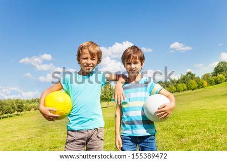 Portrait of two brothers boys stand with holding balls standing in the park on sunny summer day  Royalty-Free Stock Photo #155389472