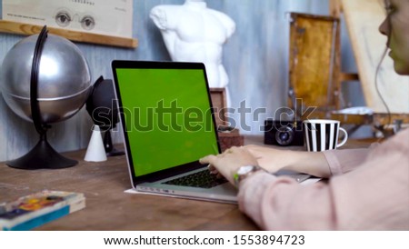 Young woman writing a text on her laptop with green screen. Stock footage. Young female employee engaged in creative work on laptop. Accelerated shooting