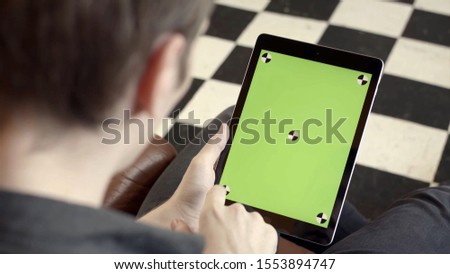 Close-up of man holding tablet and touching green screen. Stock fooatge. Young freelancer uses tablet to work or create projects. Tablet with green screen to insert