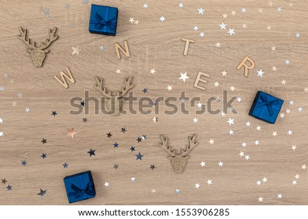 Christmas or winter wooden background with word "winter", blue boxes, golden deer heads and sparkling stars.  Flat lay, top view.Winter banner mockup,