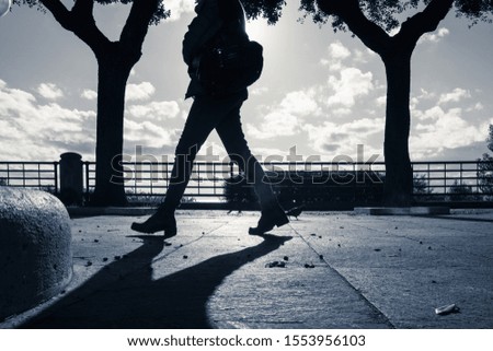 Girl in the backlight walks, the silhouette fits in the center between two trees, the shape of the trunk and large inverted branches resemble the body of the pedestrian