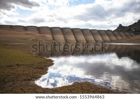 Lake with a clear water and reflective surface reflecting the dam on the horizon. Landscape of a dam and lake with beautiful colorful sky.