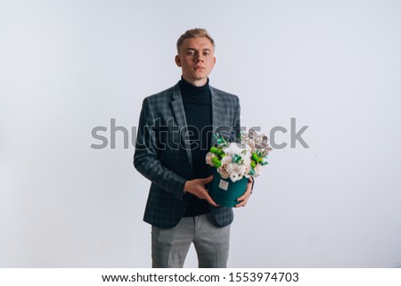 
A young guy in the image of a teacher holds a box of flowers.
Translation of the text on the wooden plate "Happy Teacher's Day."