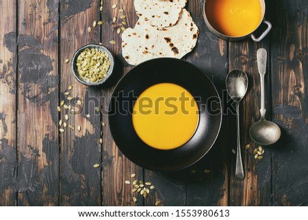 Homemade pumpkin puree soup with bread and roasted pumkin seeds over wooden background. Top view, flat lay