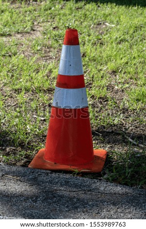 A construction cone sits alone along side the pavement. Bokeh.