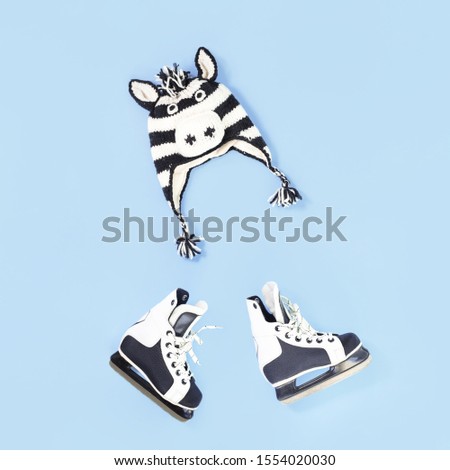 Winter is here creative concept. Zebra funny face winter hat and skates flat lay on baby blue with copy space. Seasonal activity for kids