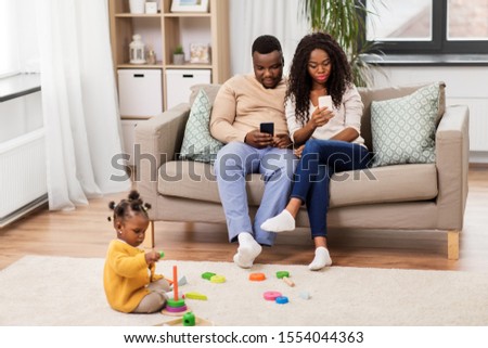 childhood and people concept - little african american baby girl playing with toy blocks and parents using smartphones at home