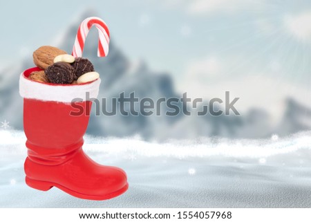 Christmas greeting card template. A red Santa boots filled with nuts and other sweets in front of a abstract blurred winter christmas landscape with mountains, snow and blue sky. Copy space.
