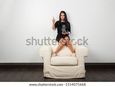 Young woman sitting on top of a couch, using a vintage medium format camera, giving direction to a scene