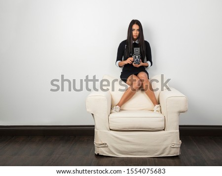 Young woman sitting on top of a couch, using a vintage medium format camera to take a phot