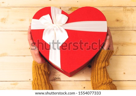 hand holding closed heart shaped box on wood table 