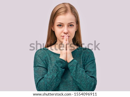 Young beautiful girl with long ginger hair with green eyes wearing sweater isolated in Studio. Gorgeous student keeps hands in praying gesture, believes in good luck at exam has calm facial expression