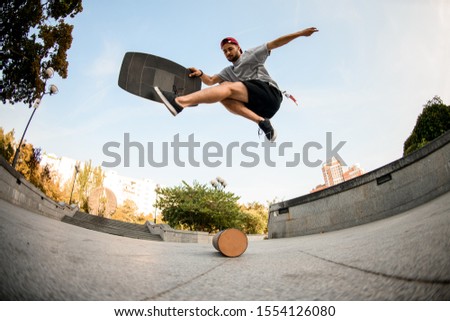 Fish-eye shot from below man making trick on the balance board on the concrete border in the background of blue clear sky