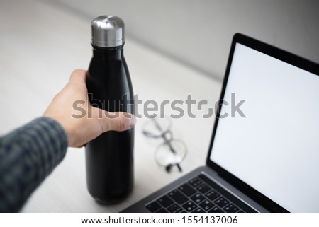Close-up of male hand take from the office desk with laptop and glasses, steel eco thermo bottle for water. Royalty-Free Stock Photo #1554137006