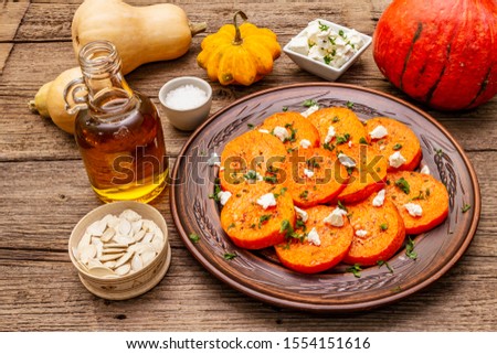 Roasted pumpkin with salted cheese and herbs. Healthy vegetarian snack. Oil, Feta, sesame seeds. Wooden boards background, copy space