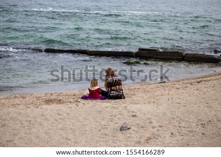 Girl with her mother on the sand by the water in autumn at sea