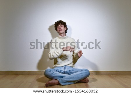 attractive and expressive Italian teenager model boy posing and gesturing barefoot for a fashion shooting wearing blue jeans and white winter turtleneck sweater