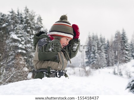 Happy child toddler, boy or girl, in snow licking  his cold hands  in winter. 