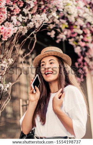 Beautiful woman with phone posing for the camera near flower composition.