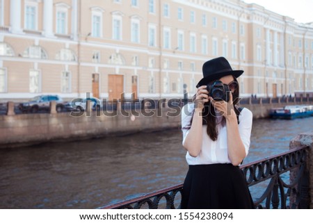 Funny hipster girl taking pictures in the city. A young woman with a hat and a camera. Tourist takes a photo of the city