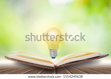 Open book and Light energy  light bulbs  Placed on a wooden floor Against the green bokeh background