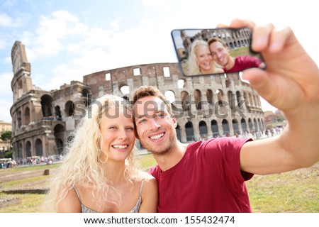 Tourist couple on travel taking pictures by Coliseum in Rome. Happy young romantic couple traveling in Italy, Europe taking self-portrait with smartphone camera in front of Colosseum. Man and woman.