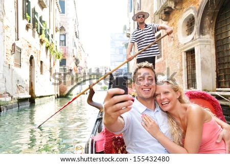 Couple in Venice on Gondola ride romance in boat happy together on travel vacation holidays. Romantic young beautiful couple taking self-portrait sailing in Venetian canal in gondola. Italy.