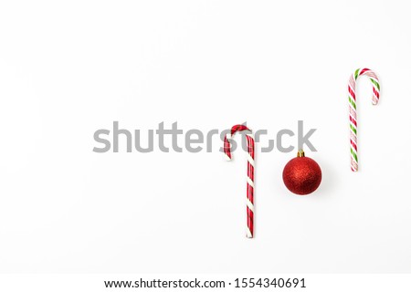 Minimal Christmas background. Traditional Christmas sweets, candy cane with red decoration bauble ball on white background