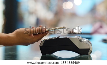 Closeup shoot a young man using his smart phone to paying with cashless wallet of e-money for POS card reader at the cashier desk. Royalty-Free Stock Photo #1554385409