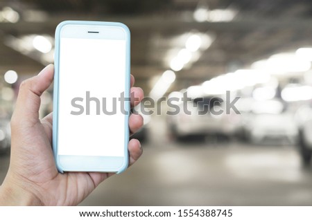 Hand with Smart phone with blank screen at parking area. Mock up image, man hands holding mobile smart phone in indoor car parking.