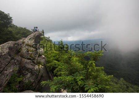 a young man sitting on the Blowing Rock on a cloudy day, North Carolina, USA