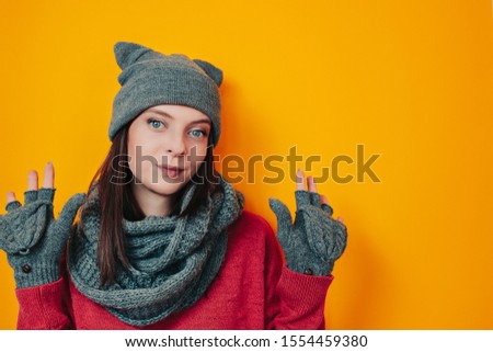 Woman in gray hat and mittens on the orange background. Young woman in sweater, hat with ears and winter gloves. Winter clothes.