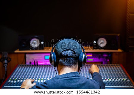 back of asian male professional music producer, sound engineer mixing a song on audio mixing console in recording studio. music production, post production concept Royalty-Free Stock Photo #1554461342