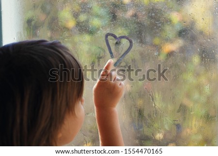Little girl draws a finger on the glass in droplets. Child painted a heart